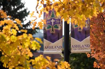 Light pole banners with the Ashland University seal surrounded by trees with fall foliage