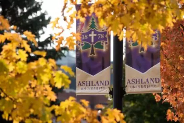 Light pole banners with the Ashland University seal surrounded by trees with fall foliage