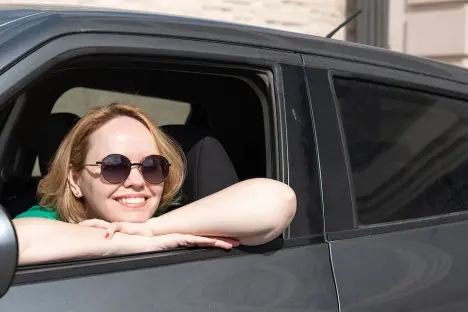 Girl sitting in her car, wearing sunglasses and smiling