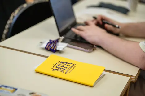 MFA notebook on desk next to hands of a person typing on their laptop computer
