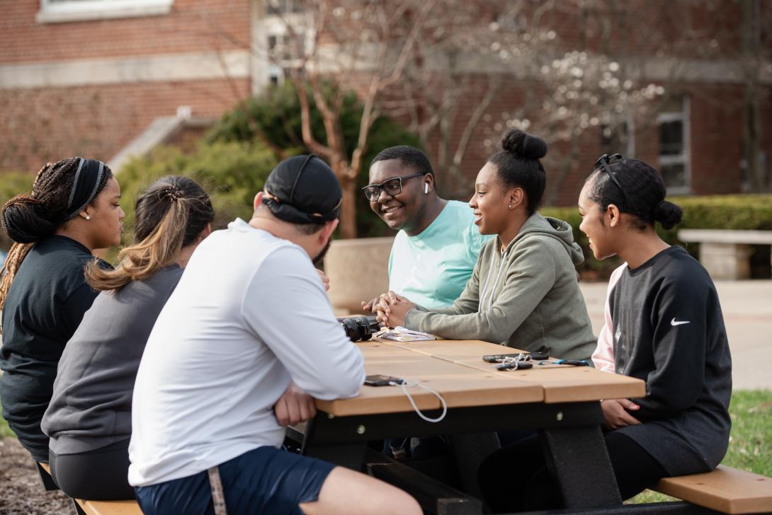 Undergraduate students sitting around a picnic table on the Quad