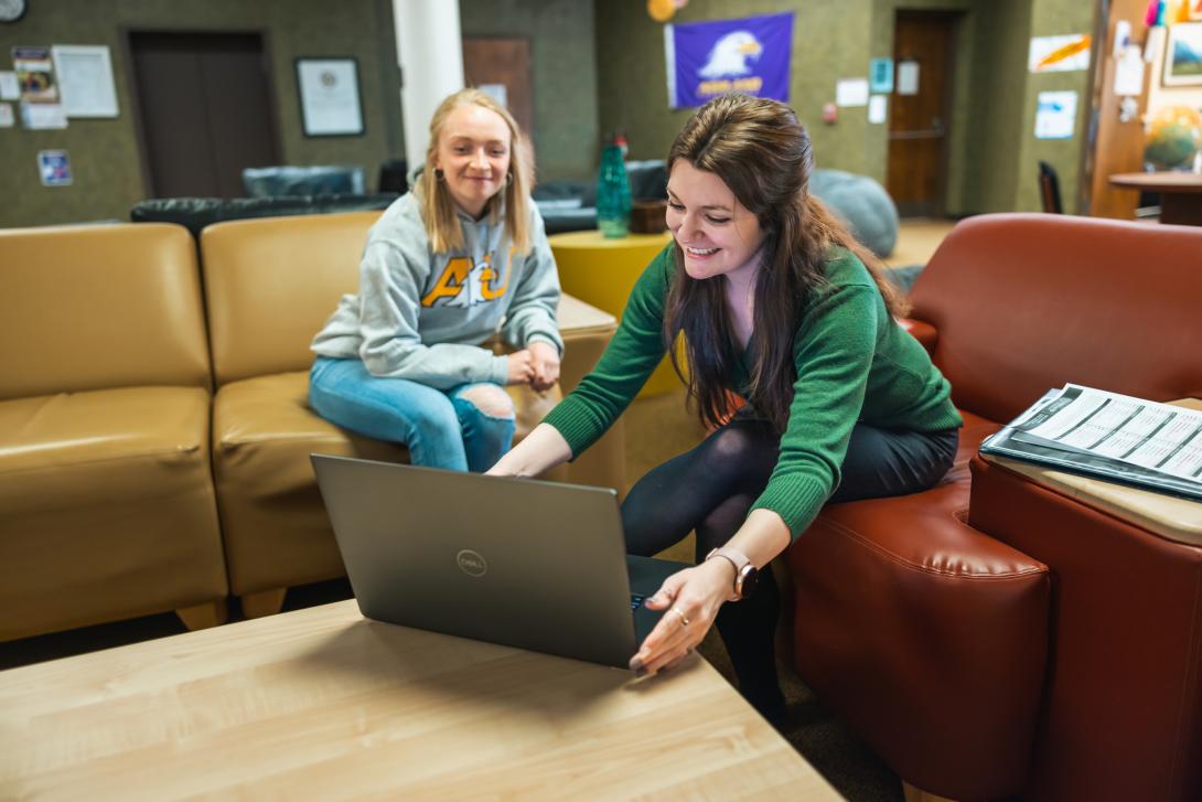 Students sitting on bench in dorm lobby working on a laptop computer