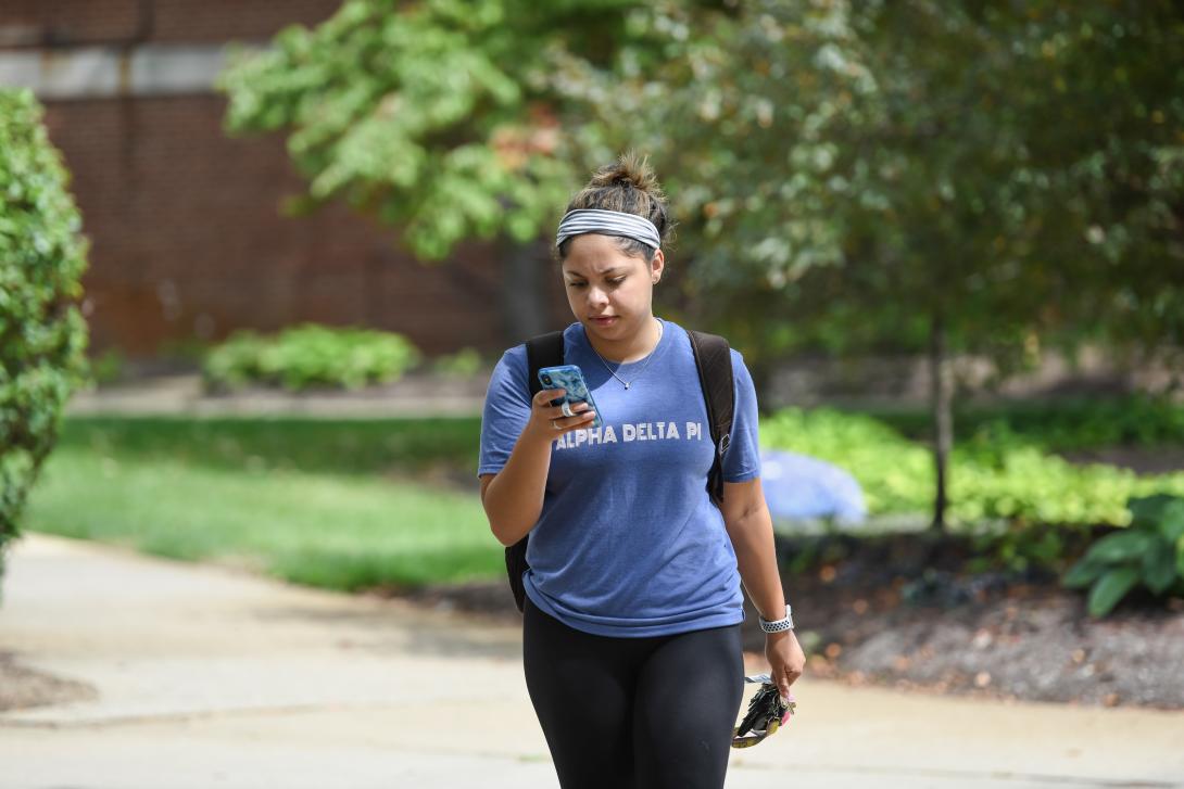 Student walking on campus looking at her cell phone