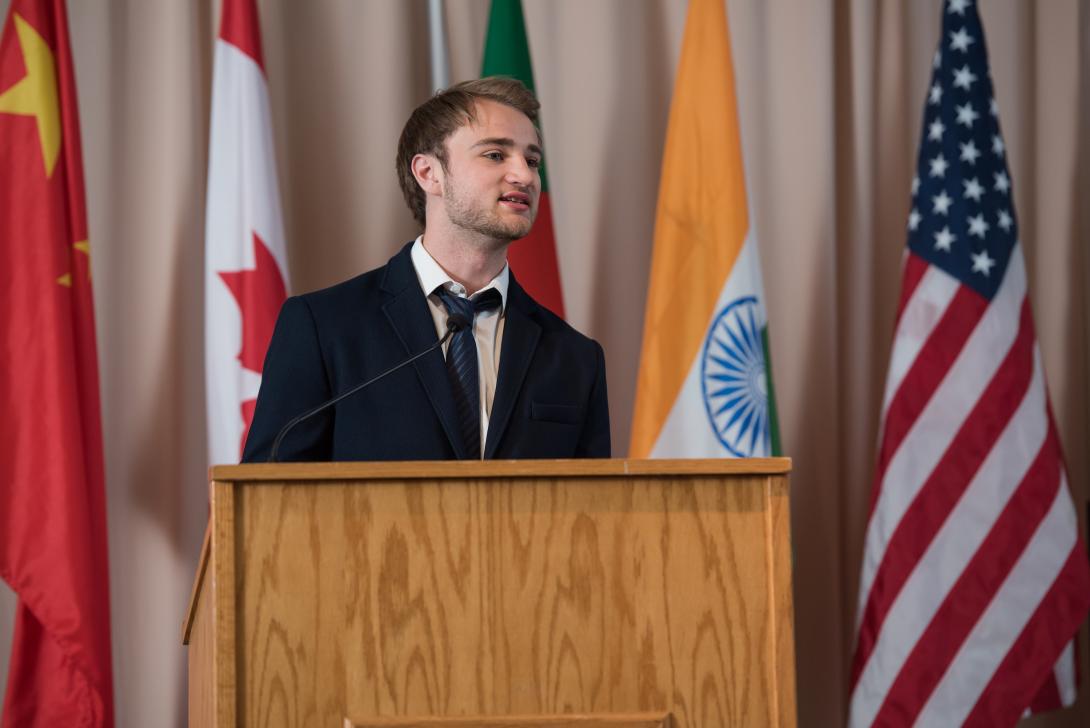 International student speaking at podium with flags from various countries in background