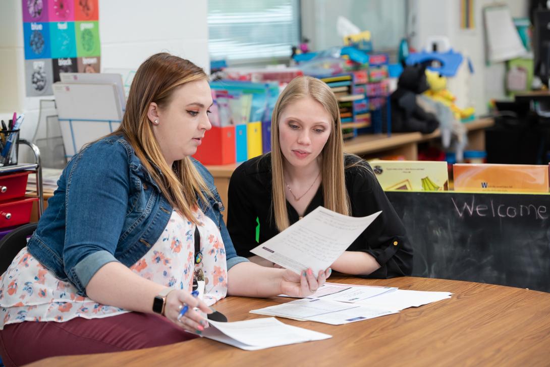 Student teacher in classroom looking over papers with teacher