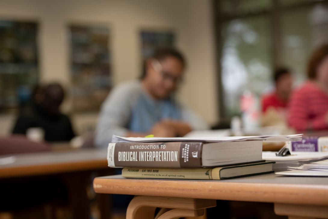 Biblical Interpretation book sitting on classroom table with students in background