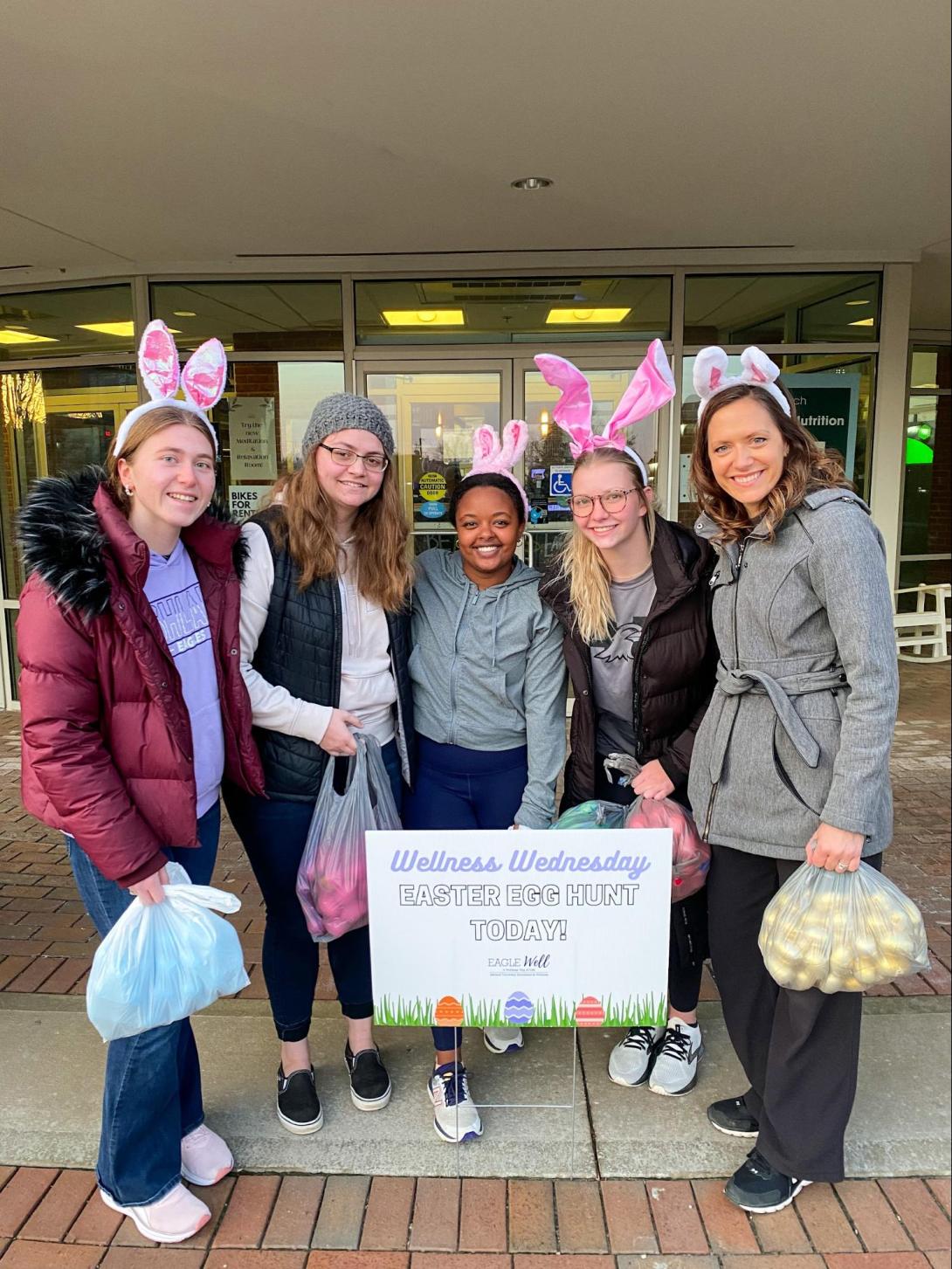 Students participating in Easter Egg Hunt, wearing bunny ears and holding bags of eggs.