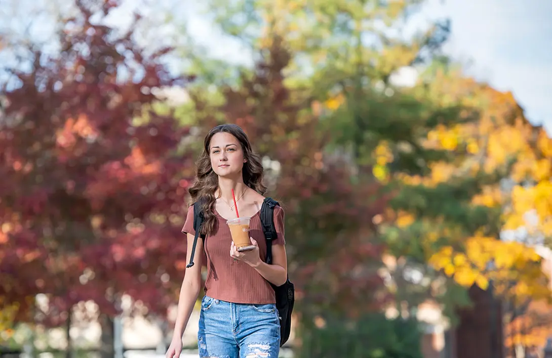 students walking with coffee in hand with fall foliage in background